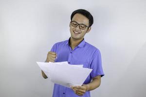 jonge aziatische man lacht en is blij als hij op een papieren document kijkt. Indonesische man met een blauw shirt. foto