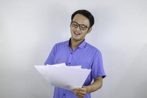 jonge aziatische man lacht en is blij als hij op een papieren document kijkt. Indonesische man met een blauw shirt. foto