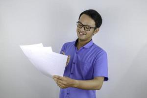 jonge aziatische man lacht en is blij als hij op een papieren document kijkt. Indonesische man met een blauw shirt. foto