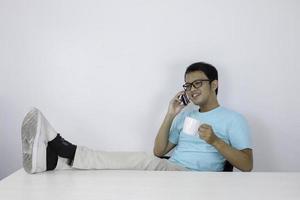 jonge aziatische man voelt zich gelukkig en lacht als hij aan de telefoon praat met een been op tafel. foto