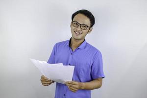 jonge aziatische man lacht en is blij als hij op een papieren document kijkt. Indonesische man met een blauw shirt. foto