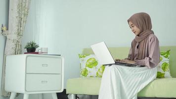 Aziatische vrouw in hijab zittend genietend van iets op haar laptop te doen foto