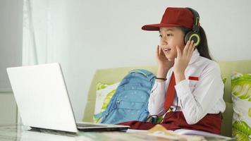 Aziatisch basisschoolmeisje dat thuis online studeert en luistert via een koptelefoon foto