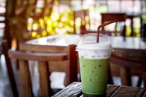 groene ijsthee of matcha latte met melkschuim in een plastic beker met bruin stro op een houten tafel in de coffeeshop met zonlicht. gezond drankje en drankconcept. foto