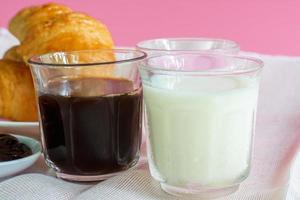 croissants geserveerd met glas verse melk, koffie op roze achtergrond. ontbijtconcept. foto