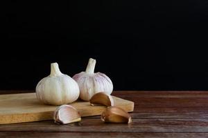 groep knoflook op snijplank en houten tafel met zwarte achtergrond. kopieer ruimte voor uw tekst. foto