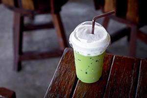 groene ijsthee of matcha latte met melkschuim in een plastic beker met bruin stro op een houten tafel in de coffeeshop. gezond drankje en drankconcept. foto