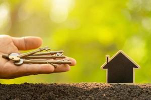 houten huis groeien in de bodem en vintage sleutel op groene natuur achtergrond wazig. sleutel tot succes over thuisbedrijf opgroeien concept foto