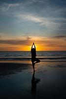 silhouet van de mens mediteren op het strand bij zonsondergang foto