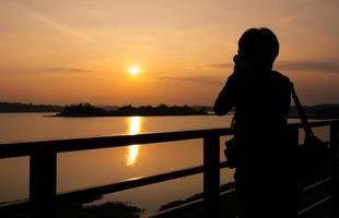 silhouet van fotograaf die foto maakt van zonsondergang over meer