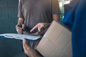 levering jonge man die aan de deur van huis staat en pakjes draagt voor een jonge man om te ondertekenen. foto