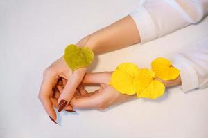 mooie vrouwelijke handen op een achtergrond, met herfstgele bladeren, het concept van zorg voor een huid van handen foto