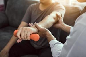 Aziatische fysiotherapeut die een patiënt helpt die dumbbells optilt om zijn herstel te doorlopen met gewichten in de kliniekkamer. foto