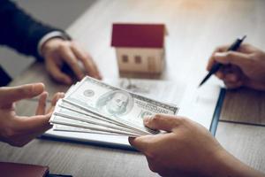investeerders gebruiken de pen op het contractpapier over het kopen van een nieuw huis terwijl ze contant geld indienen als aanbetaling voor de agent. foto
