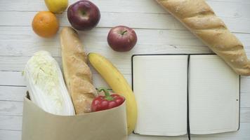 volledige papieren zak met voedingsproducten met blanco notitieboekje op houten tafel, bovenaanzicht foto