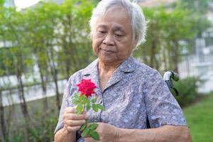 Aziatische senior of oudere oude dame vrouw met rode roos op rolstoel in park. foto