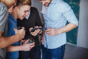 vrolijke oude vrienden communiceren met elkaar en telefoon kijken, glazen whisky in de pub. conceptentertainment levensstijl. wifi verbonden mensen in bartafelvergadering foto