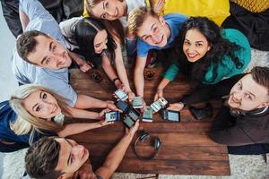 bovenaanzicht handen cirkel met behulp van telefoon in café - multiraciale vrienden mobiel verslaafd interieur scène van bovenaf - wifi verbonden mensen in bartafel vergadering - concept van teamwork foto