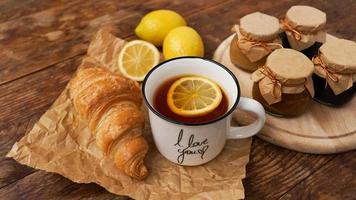 citroenthee, zelfgemaakte jam, croissant op houten tafel. ontbijtconcept. foto