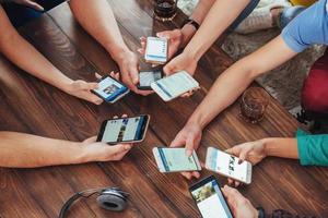 bovenaanzicht handen cirkel met behulp van telefoon in café - multiraciale vrienden mobiel verslaafd interieur scène van bovenaf - wifi verbonden mensen in bartafel vergadering - concept van teamwork foto