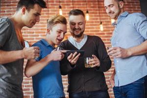 vrolijke oude vrienden communiceren met elkaar en telefoon kijken, glazen whisky in de pub. conceptentertainment levensstijl. wifi verbonden mensen in bartafelvergadering foto