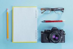 camera, bril en notitieblok en potlood op een bruine houten achtergrond foto