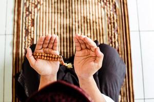 bovenaanzicht van man moslim met biddende hand op de gebedsmat terwijl hij gebedskralen vasthoudt foto