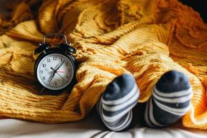 mensen slapen op een bed onder de dekens en warme sokken met wekker met 7 uur aan de zijkant foto