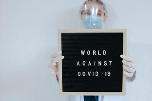 vrouwelijke arts die een beschermend masker draagt terwijl ze een citaat op een letterbord vasthoudt, zegt wereld tegen covid 19 geïsoleerd op een witte achtergrond. campagne tegen het coronavirus foto