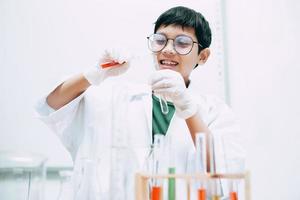 gelukkige aziatische jongensstudent met reageerbuizen die chemie studeren op schoollaboratorium, vloeistof gieten. nationale wetenschapsdag, wereldwetenschapsdag foto