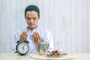 wazige foto van jonge moslimman die bidt tot god op iftar-tijd, selectieve focus op klok. traditionele ramadan, iftar-maaltijd. ramadan kareem vastenmaand concept