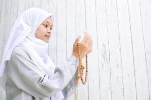 jonge Aziatische moslimvrouw die een hoofddoek draagt en bidt terwijl ze rozenkranskralen vasthoudt met kopieerruimte foto