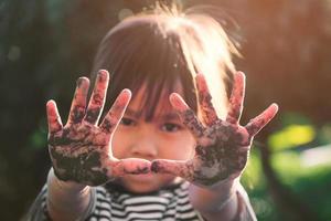 schattig klein meisje lacht en pronkt met haar modderige handen terwijl ze bomen plant in de achtertuin. onderwijsconcept buiten het schoolhek. foto