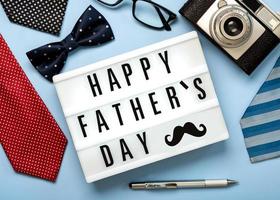 gelukkige vaderdag. lightbox met het woord gelukkige vaderdag naast stropdassen, vlinderdas, retro fotocamera, bril en pen foto