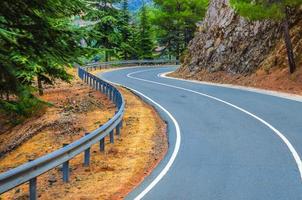 asfalt kronkelige weg in troodos-gebergte met hek langs de weg en bomen foto