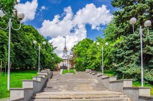 trap in groene bomensteeg met straatverlichting, politiemannenmonument en huis onder de torenspits in minsk foto