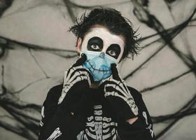 gelukkig halloween, kind met medisch masker in een skeletkostuum dat een glimlach maakt foto