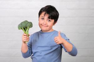 gelukkig kind met broccoli in zijn hand duim opdagen. gezond voedsel concept foto