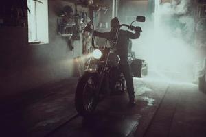 knappe brutale man met een baard zittend op een motorfiets in zijn garage foto