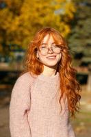 portretten van een charmant roodharig meisje met een bril en een schattig gezicht. meisje poseren in herfst park in een trui en een koraalkleurige rok. het meisje heeft een geweldige bui foto