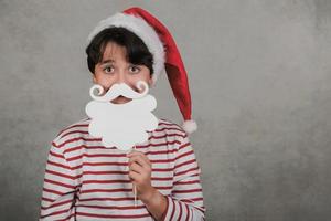 vrolijk kerstfeest, lachend kind met kerstmuts van de kerstman met valse baard op stok foto