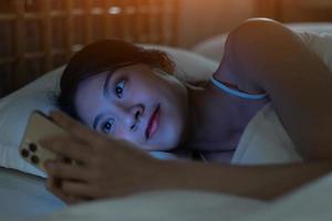 mooie jonge aziatische vrouw gebruikt smartphone om te sms'en terwijl ze zich klaarmaakt om naar bed te gaan foto