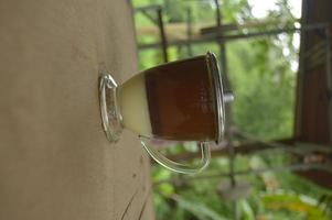 koffie serveren met een helder glas en gecondenseerde melk eronder. buiten houten achtergrond. foto