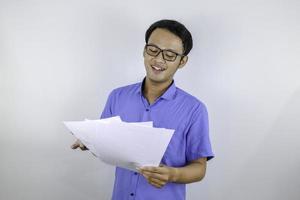 jonge aziatische man lacht en is blij als hij op een papieren document kijkt. Indonesische man met een blauw shirt. foto