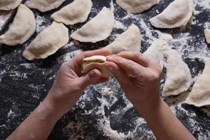 vrouw beeldhouwt dumplings met handgemaakte aardappelen op een zwarte achtergrond. vanuit de hoogste hoek geschoten. Oekraïense volkskeuken. foto