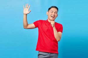 Portret van een aantrekkelijke jonge Aziatische man in een rood shirt die luid zingt terwijl hij op een blauwe achtergrond staat foto