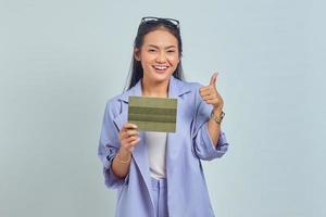 Portret van een vrolijke jonge Aziatische vrouw die een voertuigboek vasthoudt en een duim omhoog gebaar toont dat op een witte achtergrond wordt geïsoleerd foto
