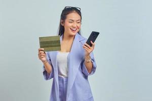 portret van vrolijke jonge aziatische vrouw die voertuigboek toont en mobiele telefoon gebruikt die op witte achtergrond wordt geïsoleerd foto