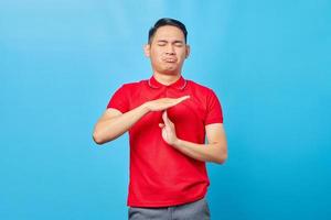 knappe jonge Aziatische man in rood shirt met time-out gebaar met handen geïsoleerd op blauwe achtergrond foto