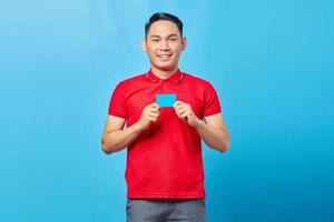 Portret van een opgewonden Aziatische jongeman die een lege creditcard toont en naar een camera kijkt die op een blauwe achtergrond wordt geïsoleerd foto